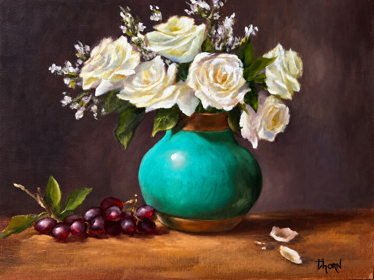 White roses in a turquoise vase with grapes and scattered petals on a wooden surface